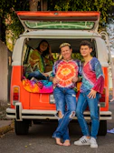 A group photo of family members dressed in colorful 90s outfits, smiling in front of a vintage camper.