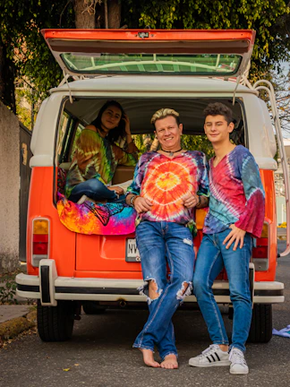 A group photo of family members dressed in colorful 90s outfits, smiling in front of a vintage camper.