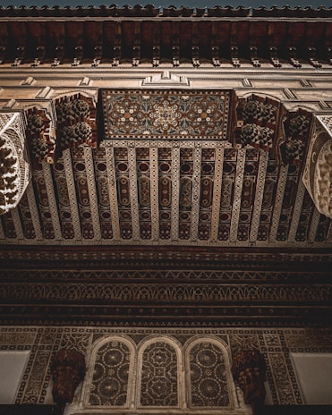 Elaborate and intricate ceiling design featuring detailed geometric patterns and floral motifs. The craftsmanship showcases ornate carvings and artistic elements typical of Moorish architecture. The woodwork is richly detailed with a variety of textures and depth.