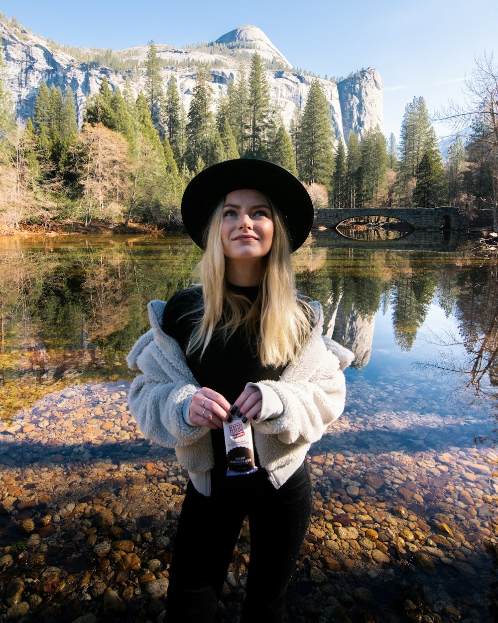 woman in gray jacket standing near lake during daytime