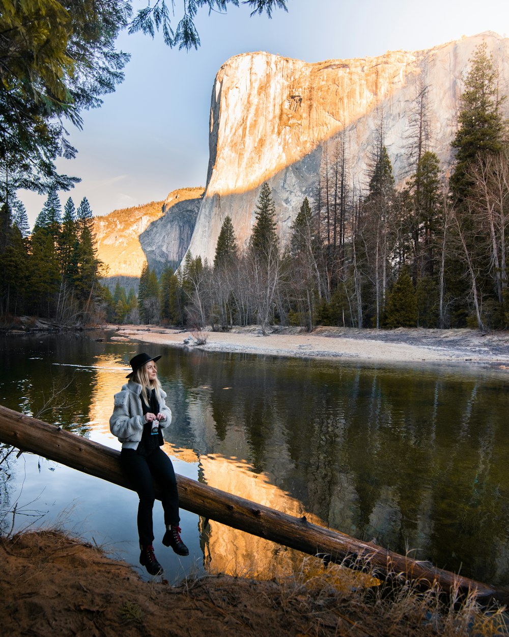 woman in gray long sleeve shirt and black pants sitting on brown wooden log near lake