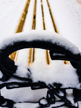Close-up of cozy winter gloves resting on a snowy wooden bench.