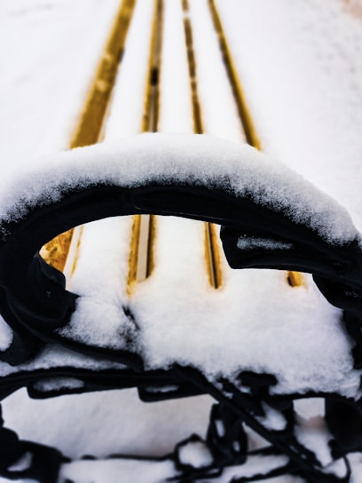 Close-up of cozy winter gloves resting on a snowy wooden bench.