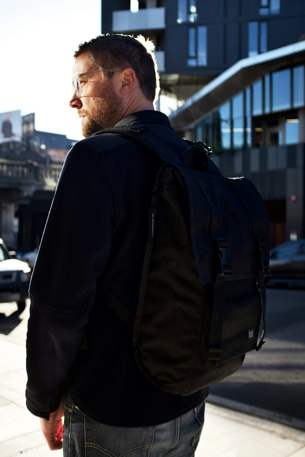man in black jacket and black backpack standing on sidewalk during daytime