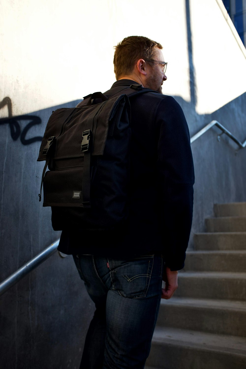 man in black jacket and blue denim jeans with black backpack standing on stairs