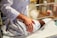 A newborn baby is gently wrapped in a patterned blanket, lying in a clear hospital bassinet. A person wearing a white coat, possibly a healthcare professional, is placing their hand on the baby, indicating care and attention. The background shows some medical equipment and supplies, signifying a hospital setting.
