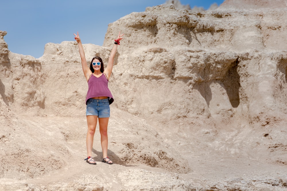 woman in blue tank top and blue denim shorts standing on brown rock formation during daytime