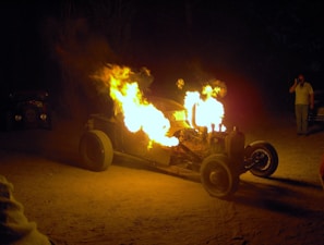 A gleaming vintage hot rod with flames painted on the sides parked under string lights at dusk
