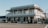 A two-story historic hotel building with a veranda and classic architectural design, featuring white wooden paneling and balconies. There are outdoor seating areas with tables and chairs under umbrellas, surrounded by potted plants.