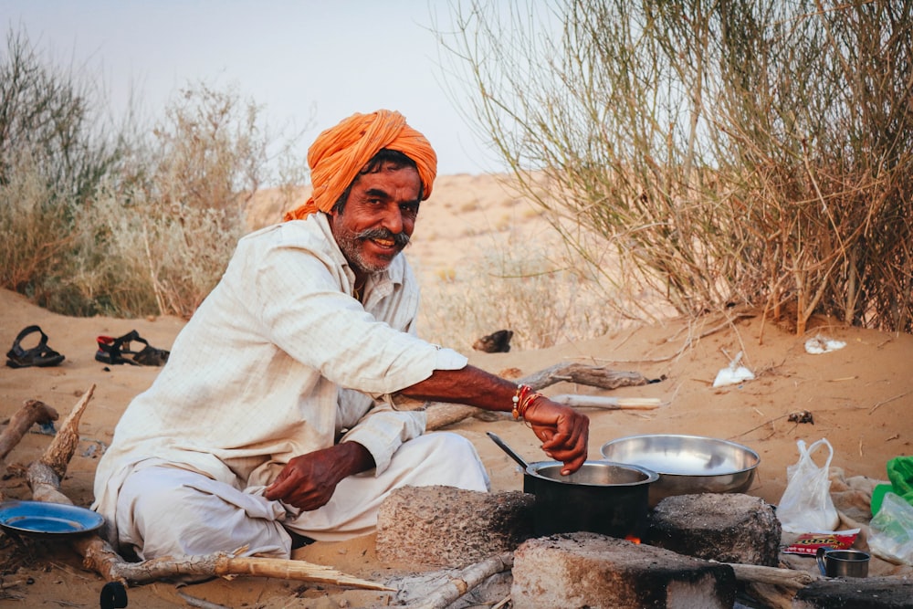 woman in white robe sitting on brown rock near black cooking pot during daytime