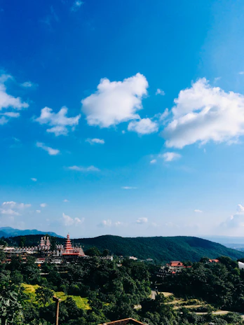 Scenic view of a peaceful temple surrounded by lush greenery and pilgrims walking towards it.