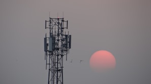 A towering telecom mast under construction with workers securing cables at sunset