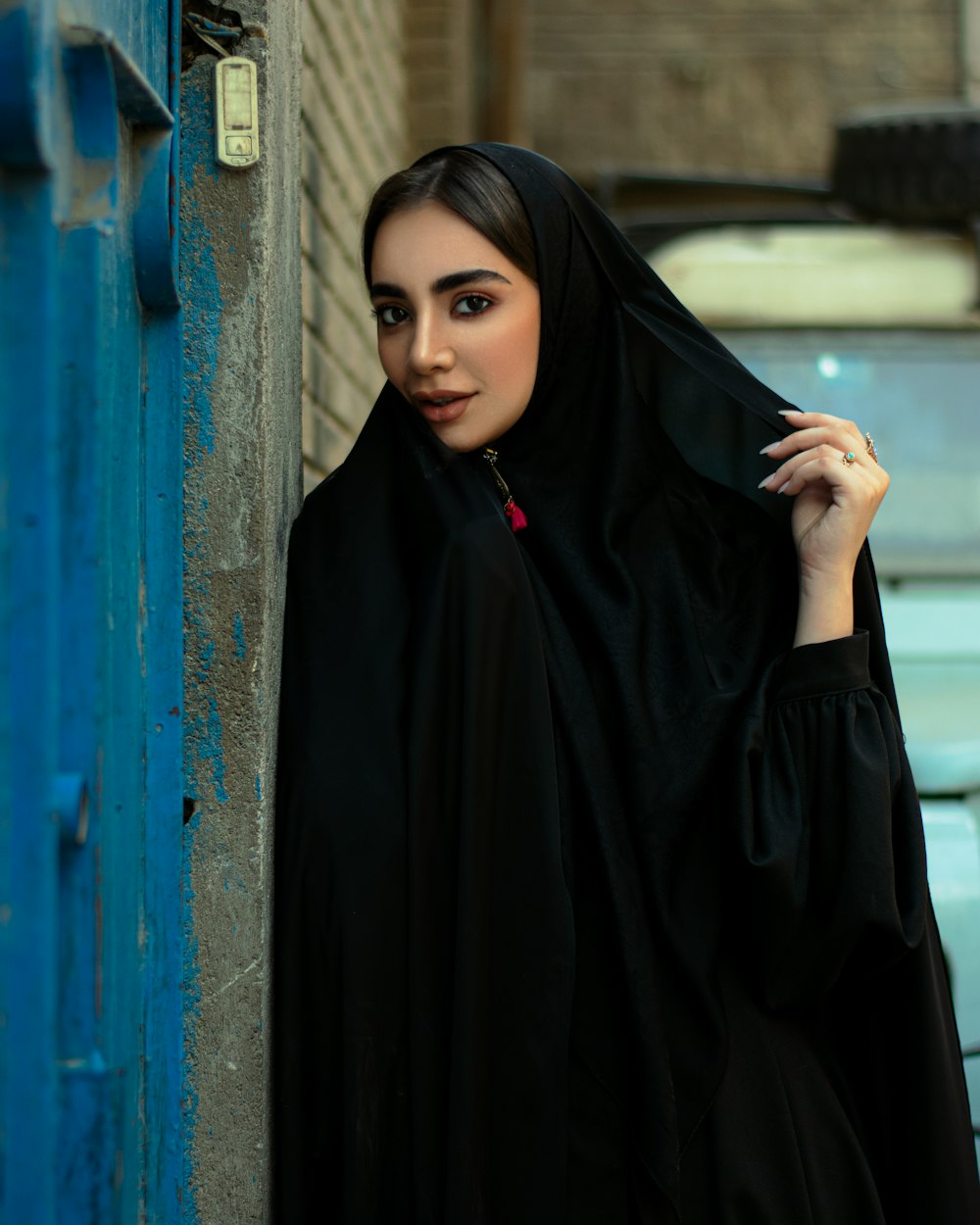 woman in black hijab standing beside blue wall