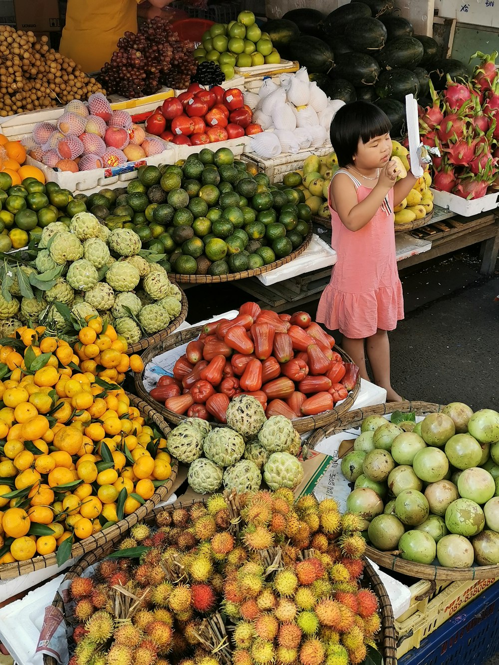 Mujer en camisa rosa de manga larga de pie junto a las frutas