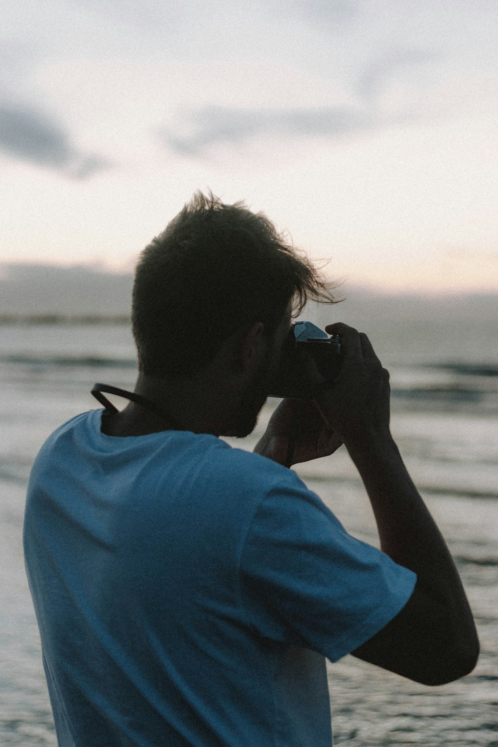 man in blue shirt taking photo of sea during daytime