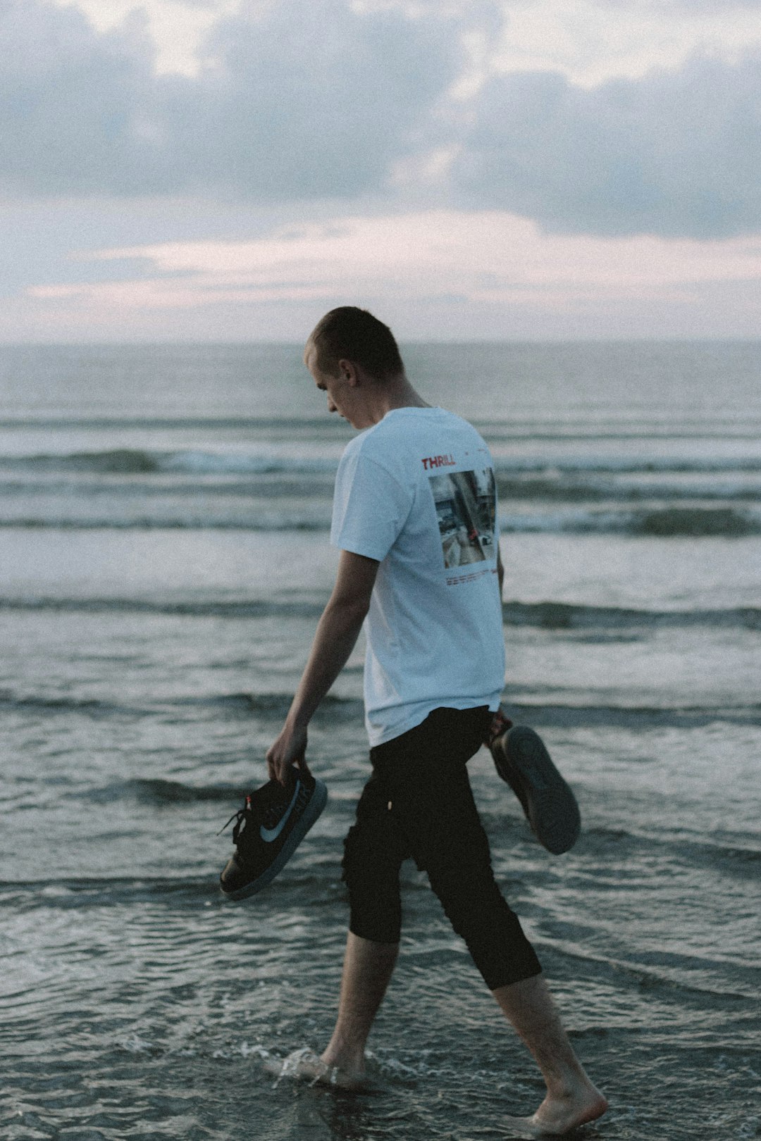 man in white t-shirt and black pants holding black and white surfboard on sea shore