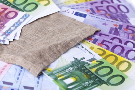 A spread of various Euro banknotes ranging from 10 to 500 denominations with a brown burlap sack placed on top of them.