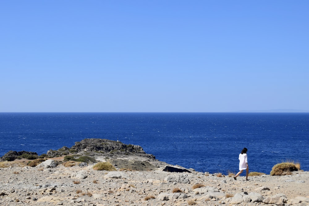 woman in white shirt standing on brown sand near body of water during daytime