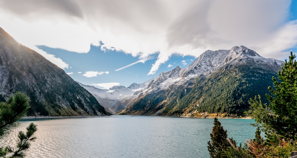 green trees near lake and mountains under white clouds and blue sky during daytime