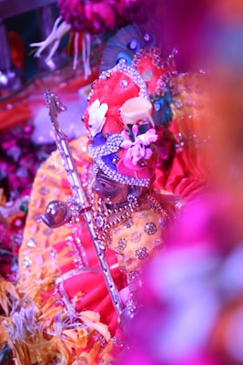 An elaborately dressed and decorated idol wearing vibrant, colorful garments and ornaments. The figure holds a flute and is surrounded by floral decorations, creating a rich and festive atmosphere.