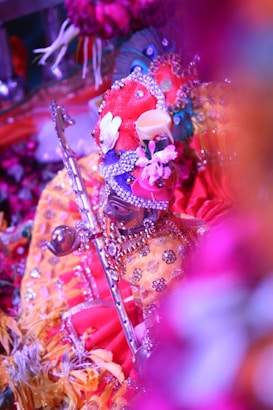 An elaborately dressed and decorated idol wearing vibrant, colorful garments and ornaments. The figure holds a flute and is surrounded by floral decorations, creating a rich and festive atmosphere.