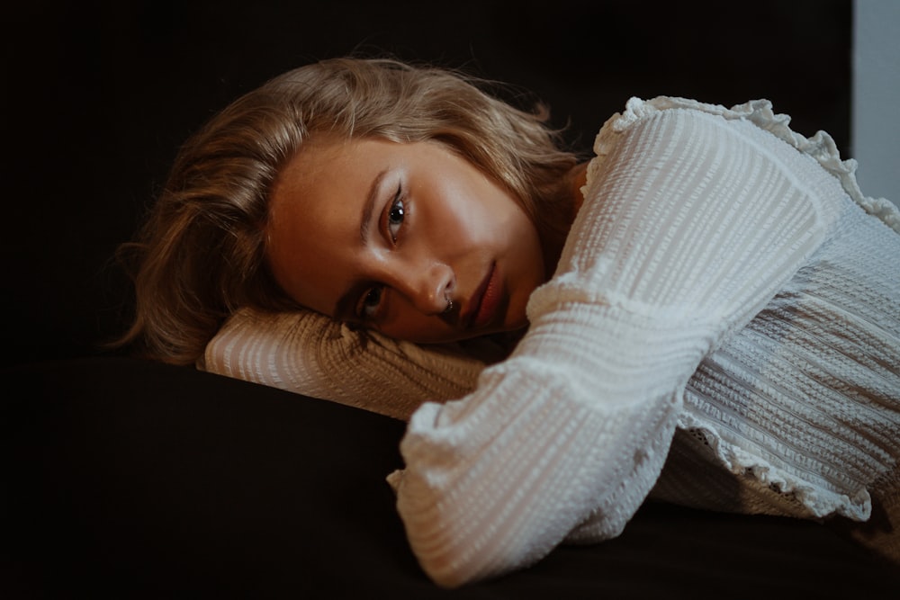 woman in white knit sweater lying on black textile