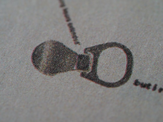 A close-up view of a printed image showing a bottle opener, created with a dot matrix pattern. The dots are densely packed, giving the image a textured appearance on a light-colored background.