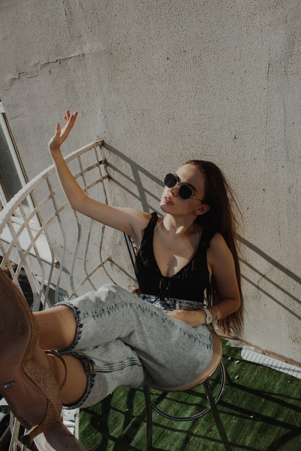 woman in black tank top and blue denim jeans wearing black sunglasses sitting on white metal