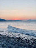 Waves gently lapping against a rocky shore under a pastel sunset.