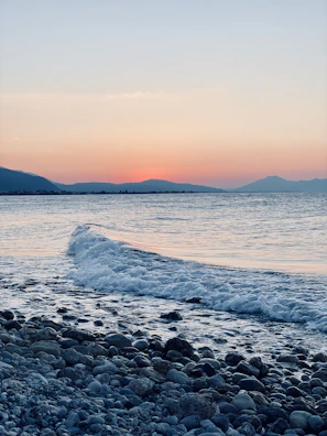 Waves gently lapping against a rocky shore under a pastel sunset.