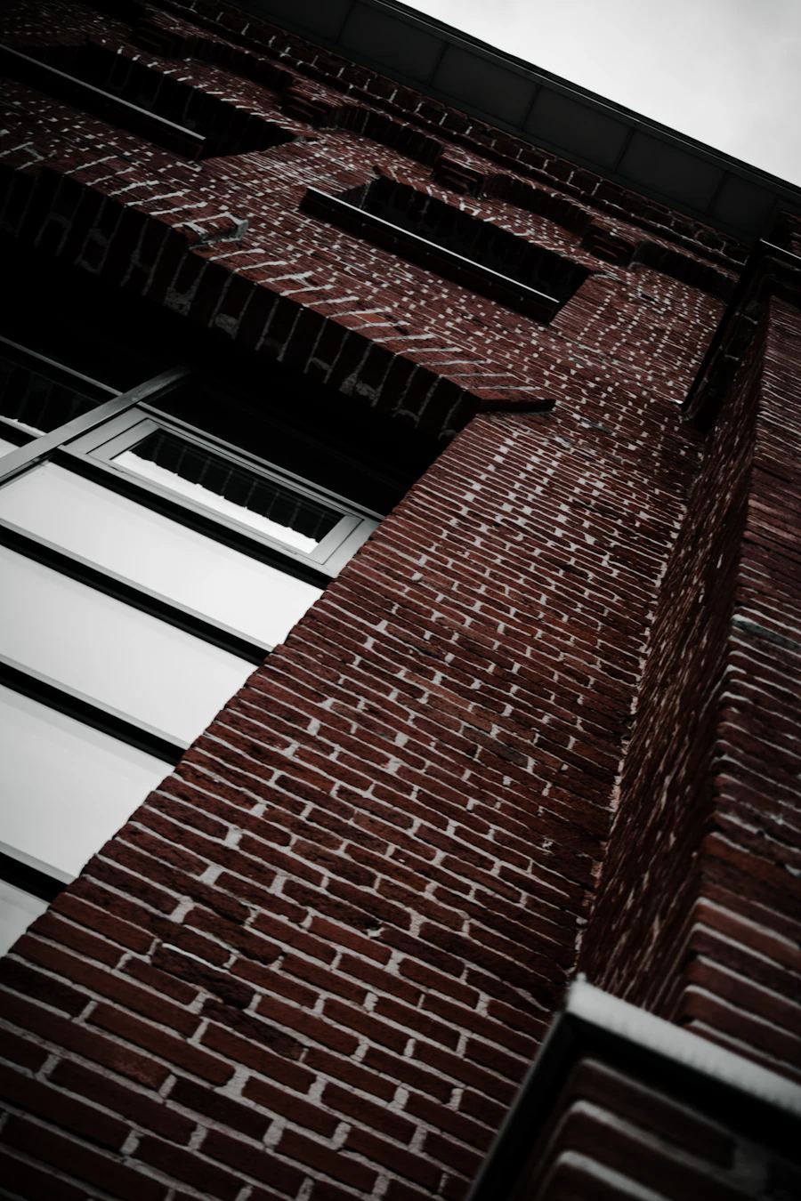 Dark brick wall beside a run of angled glazing on a modern building