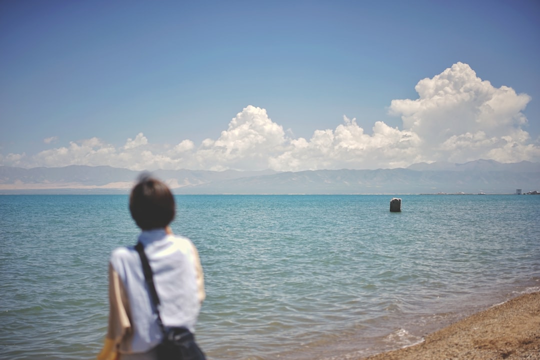 woman in white shirt standing on seashore during daytime