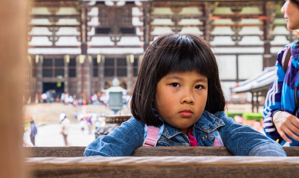 昼間、茶色の木製のベンチに座るブルーデニムジャケットの女の子