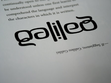 The image features the name 'Galileo' written in a unique, artistic style with stylized fonts. The text appears to be in black ink on a white paper background, positioned at an angle. Above it, there are lines of regular printed text and below is a mention of Galileo Galilei's full name in a smaller font.
