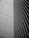 A modern architectural facade featuring a sleek grid pattern with vertical lines and rectangular shapes. The image depicts the convergence of two building sides, one with a tiled texture and the other with metal slats, creating a sense of order and precision.