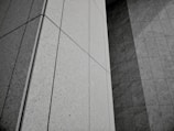 Geometric patterns formed by concrete or stone tiles arranged in a grid-like pattern. The surface features clean lines and large rectangular panels with a mix of textures.