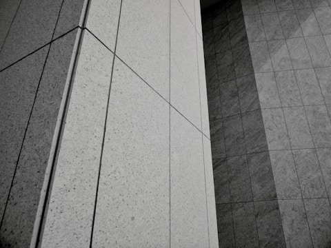 Geometric patterns formed by concrete or stone tiles arranged in a grid-like pattern. The surface features clean lines and large rectangular panels with a mix of textures.