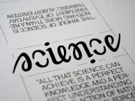 A close-up view of a typography artwork featuring the word 'science' in a stylized, script-like black font against a white background. Below it, there is a quote about science written in a smaller, sans-serif font. Above the main word, there is another sentence printed upside-down.
