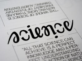 A close-up view of a typography artwork featuring the word 'science' in a stylized, script-like black font against a white background. Below it, there is a quote about science written in a smaller, sans-serif font. Above the main word, there is another sentence printed upside-down.