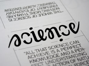 A close-up view of a typography artwork featuring the word 'science' in a stylized, script-like black font against a white background. Below it, there is a quote about science written in a smaller, sans-serif font. Above the main word, there is another sentence printed upside-down.
