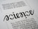 A close-up view of a typography artwork featuring the word 'science' in a stylized, script-like black font against a white background. Below it, there is a quote about science written in a smaller, sans-serif font. Above the main word, there is another sentence printed upside-down.