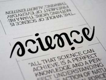 A close-up view of a typography artwork featuring the word 'science' in a stylized, script-like black font against a white background. Below it, there is a quote about science written in a smaller, sans-serif font. Above the main word, there is another sentence printed upside-down.