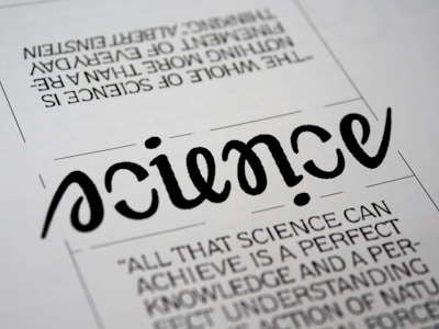 A close-up view of a typography artwork featuring the word 'science' in a stylized, script-like black font against a white background. Below it, there is a quote about science written in a smaller, sans-serif font. Above the main word, there is another sentence printed upside-down.