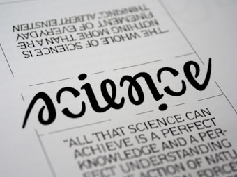 A close-up view of a typography artwork featuring the word 'science' in a stylized, script-like black font against a white background. Below it, there is a quote about science written in a smaller, sans-serif font. Above the main word, there is another sentence printed upside-down.
