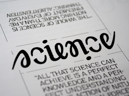A close-up view of a typography artwork featuring the word 'science' in a stylized, script-like black font against a white background. Below it, there is a quote about science written in a smaller, sans-serif font. Above the main word, there is another sentence printed upside-down.