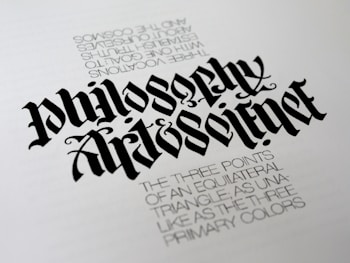A piece of calligraphy art displaying stylized, elaborately designed text. The primary focus is the words 'Philosophy' and 'Art & Science' written in a bold, gothic font. Beneath, there is smaller printed text describing concepts related to equilateral triangles and primary colors, adding a philosophical dimension.
