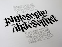 A piece of calligraphy art displaying stylized, elaborately designed text. The primary focus is the words 'Philosophy' and 'Art & Science' written in a bold, gothic font. Beneath, there is smaller printed text describing concepts related to equilateral triangles and primary colors, adding a philosophical dimension.