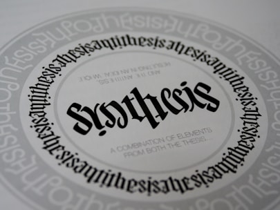 A detailed and symmetrical text design with the word 'synthesis' prominently displayed in the center in a gothic-style font. The word is surrounded by circular text patterns repeating the word 'synthesis' in a smaller font size, creating a visually hypnotic effect. Smaller text underneath the central word reads 'A combination of elements from both the thesis...'