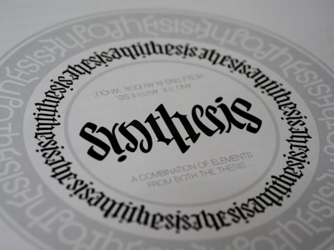A detailed and symmetrical text design with the word 'synthesis' prominently displayed in the center in a gothic-style font. The word is surrounded by circular text patterns repeating the word 'synthesis' in a smaller font size, creating a visually hypnotic effect. Smaller text underneath the central word reads 'A combination of elements from both the thesis...'