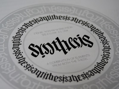 A detailed and symmetrical text design with the word 'synthesis' prominently displayed in the center in a gothic-style font. The word is surrounded by circular text patterns repeating the word 'synthesis' in a smaller font size, creating a visually hypnotic effect. Smaller text underneath the central word reads 'A combination of elements from both the thesis...'